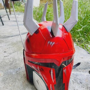 May include: A red and black helmet with white detailing, showcasing a unique design with several upward-facing protrusions. The helmet is likely a prop or costume element, potentially inspired by science fiction or fantasy.