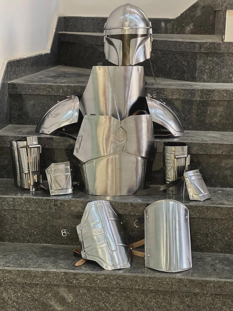May include: A complete set of polished silver armor, including a helmet, chest plate, shoulder pads, and various other protective pieces. The armor is displayed on a set of gray steps, showcasing its intricate design and metallic sheen.