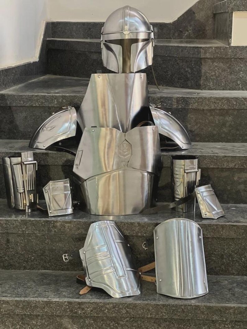 May include: A complete set of polished metal armor, including a helmet, chest plate, shoulder guards, arm and leg pieces. The armor is displayed on a set of gray steps, showcasing its intricate design and reflective surface.