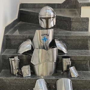 May include: A complete set of polished metal armor, including a helmet, chest plate, shoulder pads, and leg and arm guards. The chest plate features the text "ZEHRA HANDICRAFTS" with a star emblem. The armor is displayed on a set of stairs.