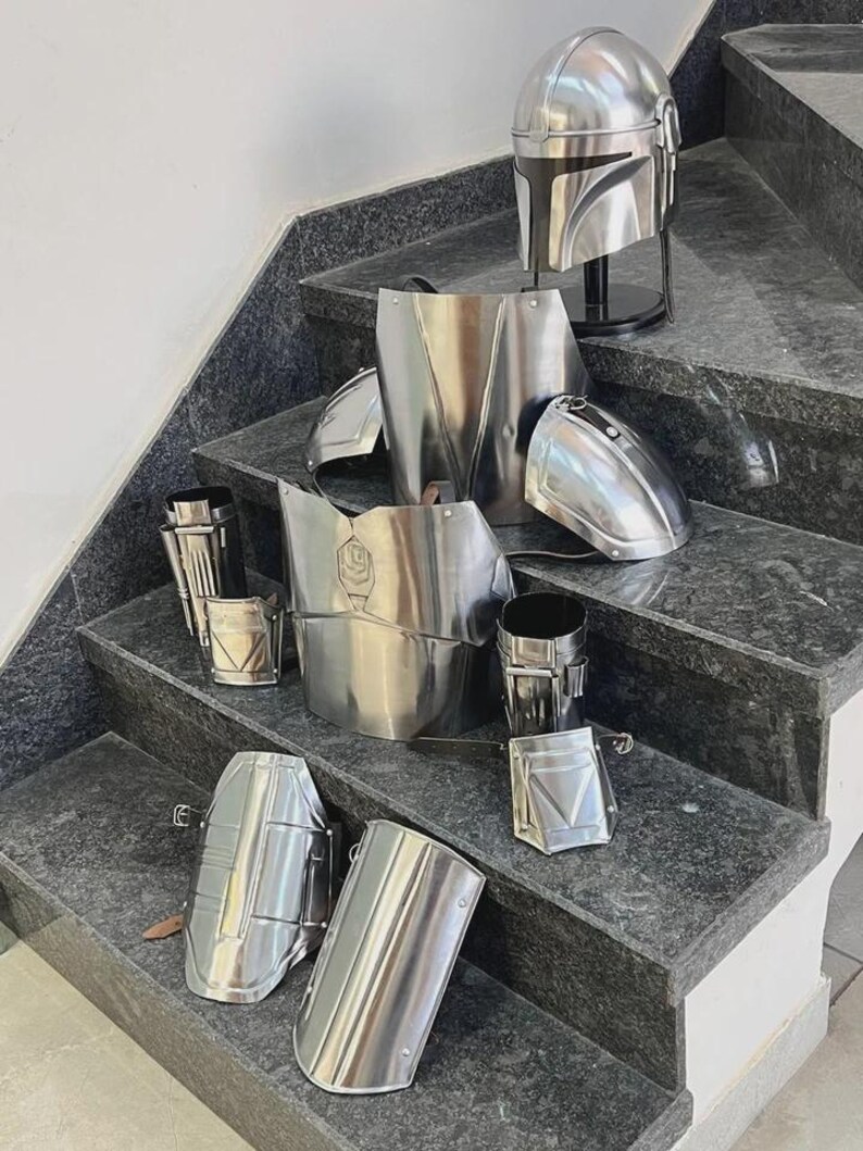 May include: A collection of shiny, silver metal armor pieces, including a helmet, chest plate, and various arm and leg guards. The armor is displayed on a set of gray stairs, showcasing the detailed craftsmanship and design of the costume.