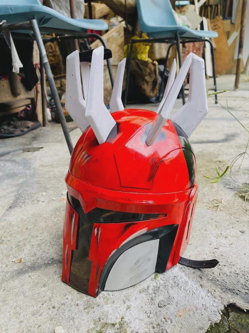 May include: A red and black helmet with white horns. The helmet has a visor and a chin strap. The helmet is likely a costume or prop.