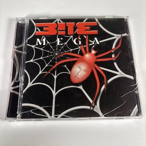 Peut inclure: Un boîtier de CD avec l'album "B!TE MEGA". La pochette présente une araignée rouge avec un visage sur fond noir avec un motif de toile d'araignée blanche. Le titre de l'album est en rouge et blanc.