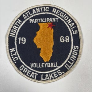 Op de afbeelding: Een ronde patch met een marineblauwe achtergrond en wit geborduurde tekst. De patch leest "North Atlantic Regionals" en "Great Lakes Illinois" rond de rand. Een goudkleurige Illinois-omtrek staat in het midden, met ook "1968" en "Volleyball".