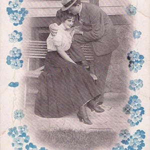 Peut inclure: Carte postale vintage représentant un couple s'embrassant. L'homme porte un costume et un chapeau, la femme une jupe et un chemisier. Des motifs floraux bleus encadrent l'image, avec le texte : "Birds of a feather flock together. Come, let's flock!"