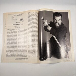 May include: A black and white photograph from a magazine shows a man holding a sword, with an intense expression. The magazine pages include the text "THE CRITICS" and "RUNNING WILD".