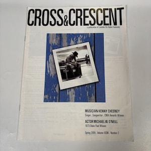 May include: The Cross & Crescent magazine, a publication of Lambda Chi Alpha Fraternity, features a black and white photo of a person in a cowboy hat sitting on a crate against a blue wood background. Text includes Kenny Chesney and Michael W. O'Neill.
