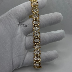 Könnte beinhalten: Ein goldfarbenes Armband mit ovalen Gliedern, die mit kleinen, funkelnden Edelsteinen besetzt sind. Die Glieder sind durch ein X-förmiges Design verbunden. Der Text "SB GEMS" ist sichtbar.