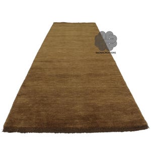 May include: A rectangular brown rug with a textured surface. The rug is long and narrow, suitable for a hallway or entryway. The rug has a simple, solid color design. The logo "NAZMACREATIONS" is visible in the upper right corner.