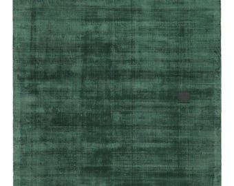 May include: A rectangular, emerald green rug with a textured surface. The rug has a subtle, distressed appearance, with variations in the green hue. A small, dark square is visible near the top center of the rug.