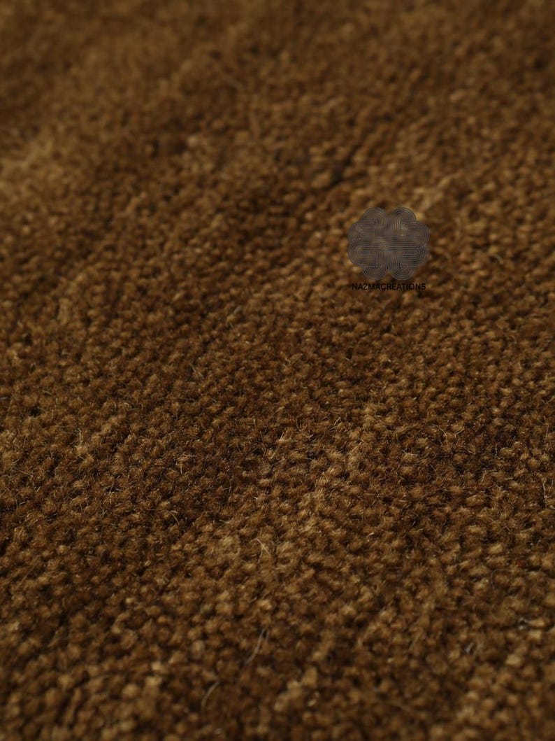 May include: Close-up of a brown, textured rug. The rug has a dense, looped pile, creating a soft, inviting appearance. The color is a warm, earthy brown, suitable for home decor.