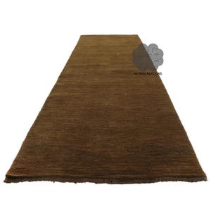 May include: A rectangular brown rug with a textured surface. The rug is a solid color and appears to be made of a woven material. The rug is displayed on a white background. The text "NAZMACREATIONS" is visible on the rug.