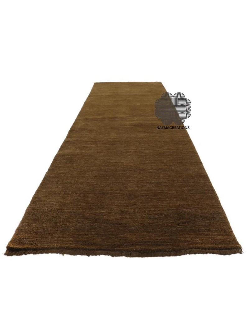 May include: A rectangular brown rug with a textured surface. The rug is a solid color and appears to be made of a woven material. The rug is displayed on a white background. The text "NAZMACREATIONS" is visible on the rug.
