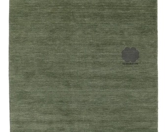 May include: A rectangular, olive green rug with a textured surface. The rug has a simple design and a subtle sheen. The bottom right corner features a dark gray emblem with the text "HAZMACREATIONS".