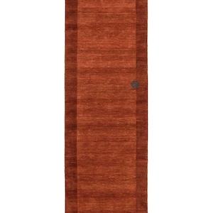 May include: A rectangular, rust-colored rug with a darker border. The rug has a simple, modern design and a textured surface. A small, circular detail is visible on the right side of the rug. This rug is suitable for a hallway or entryway.