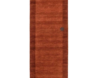 May include: A rectangular, rust-colored rug with a darker border. The rug has a simple, modern design and a textured surface. A small, circular detail is visible on the right side of the rug. This rug is suitable for a hallway or entryway.