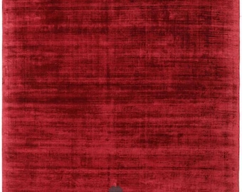 Puede incluir: Una alfombra roja rectangular grande con una superficie texturizada. La alfombra tiene un aspecto oscuro y moteado con estrías horizontales. Una pequeña mancha gris oscuro es visible cerca del centro de la alfombra.