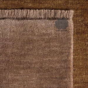May include: Close-up of three textured rugs in shades of brown. The top rug is a dark brown, the middle rug is a lighter brown, and the bottom rug is a medium brown. Each rug has a fringed edge. The tag on the bottom rug reads "NAZMACREATIONS".