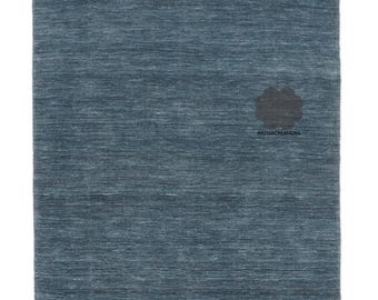 Puede incluir: Una alfombra rectangular azul sólido con una superficie texturizada. La alfombra tiene un patrón horizontal sutil y una franja en el borde superior. El logotipo "NAZMACREATIONS" es visible en la esquina inferior derecha.
