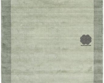 May include: A rectangular area rug in shades of green. The rug has a light green center with a darker green border. The texture appears soft and plush. The logo "NAZMACREATIONS" is in the lower right corner.