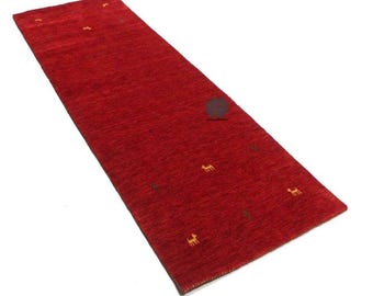 May include: A long, rectangular red rug with small, repeating yellow animal figures and a dark brown circular design. The rug has a textured surface and is likely made of woven material.
