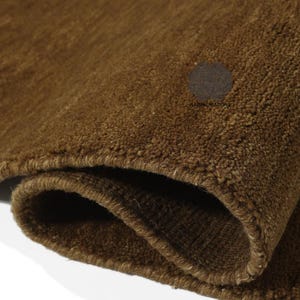 May include: Close-up of a rolled-up brown rug. The rug has a thick, textured pile and a warm, earthy tone. The edges are neatly finished, and the overall appearance suggests a high-quality, durable product. The rug's color is consistent throughout.