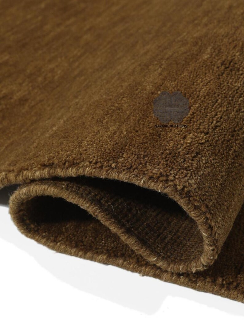 May include: Close-up of a rolled-up brown rug. The rug has a thick, textured pile and a warm, earthy tone. The edges are neatly finished, and the overall appearance suggests a high-quality, durable product. The rug's color is consistent throughout.
