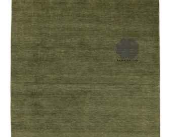 May include: A rectangular olive green rug with a textured surface. The rug has a solid color and a simple design. The bottom edge has a slightly darker green border. The rug has the text "NAZMACREATIONS" in the lower right corner.