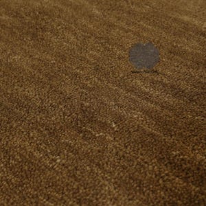 May include: Close-up of a brown rug with a textured surface. The rug has a dense, plush pile, creating a soft, inviting appearance. The color is a warm, earthy brown, with subtle variations in tone. The rug is likely for home decor.