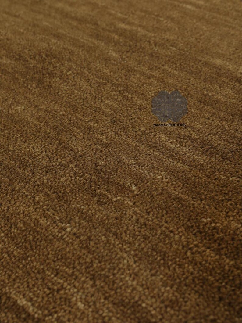 May include: Close-up of a brown rug with a textured surface. The rug has a dense, plush pile, creating a soft, inviting appearance. The color is a warm, earthy brown, with subtle variations in tone. The rug is likely for home decor.