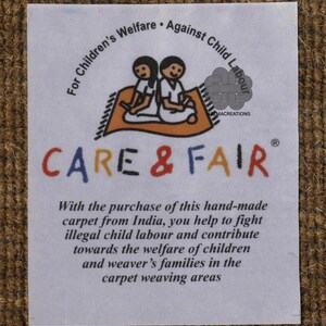 May include: A white label with text and a graphic of two children on a carpet. The label reads "CARE & FAIR" and promotes the purchase of handmade carpets from India to fight child labor and support children's welfare.