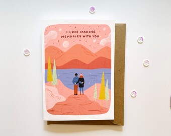 May include: Greeting card with a landscape illustration featuring two figures embracing, overlooking a lake and mountains under a starry sky. The card reads "I love making memories with you." Includes a brown envelope.