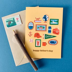 May include: A yellow Father's Day card with illustrations of a globe, fish, and radio, with the text "happy father's day." A brown pencil, envelope, and a vintage postage stamp are also visible.