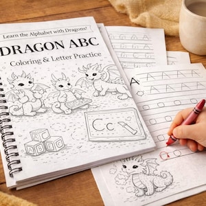 May include: A spiral-bound "Dragon ABC" coloring and letter practice book with dragon illustrations. The book is open, with a child's hand holding a red crayon, practicing writing letters. Includes colorful crayons and alphabet blocks.