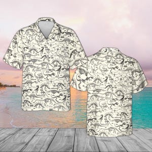 Puede incluir: Camisa de manga corta con fondo crema y estampado de esqueletos de dinosaurios negros. La camisa tiene cuello clásico y corte relajado, perfecta para uso diario. El diseño incluye varias especies de dinosaurios.