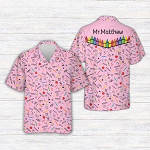 May include: A short-sleeve button-down shirt in light pink featuring a repeating pattern of school-themed icons including crayons, apples, math equations, and the text 'ABC' and 'Teacher'. The back yoke displays 'Mr.Matthew' above a row of crayons.