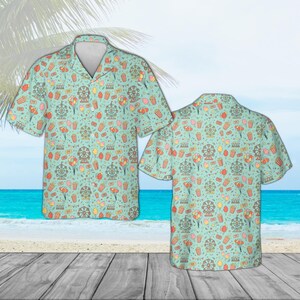 May include: Two short-sleeved button-down shirts with a light teal background. The shirts feature a repeating pattern of carnival-themed icons, including Ferris wheels, popcorn, balloons, and cotton candy. The shirts are displayed on a wooden surface with a beach and ocean background.
