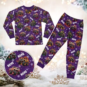 May include: A long-sleeve shirt and pants pajama set in purple featuring a repeating pattern of monster trucks, white snowflakes, and the word NAME printed in white. The monster trucks are decorated with holiday elements like Santa hats.