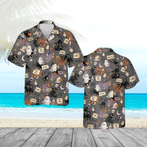 May include: A short-sleeve button-down shirt in dark gray featuring an all-over Halloween print. The pattern includes black cats, white ghosts, lit candles, potion bottles, and text labels reading "Spooky," "Cozy," "Boo," and "Trick or Treat."