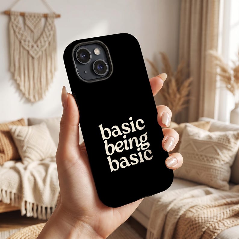 May include: A black smartphone case featuring the white text "basic being basic" printed in a bold, rounded serif font. The case has a cutout for a dual-lens camera system on the back, showcasing a sleek, solid-colored design for mobile devices.