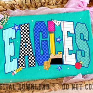 May include: A teal t-shirt featuring the word EAGLES in large block letters. Each letter has a unique pattern including stripes, black and white checkers, blue checkers, a yellow pencil, and notebook paper. Small stars, a paper airplane, and an apple are included.