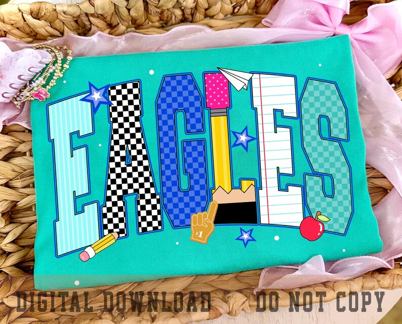 May include: A teal t-shirt featuring the word EAGLES in large block letters. Each letter has a unique pattern including stripes, black and white checkers, blue checkers, a yellow pencil, and notebook paper. Small stars, a paper airplane, and an apple are included.