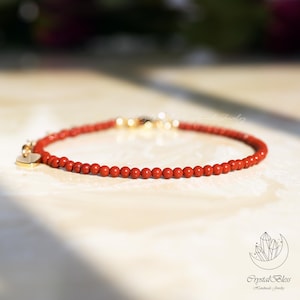 May include: Red beaded bracelet with a gold heart charm and clasp. The bracelet features small, round red beads strung together. The gold heart charm hangs delicately from the bracelet, adding a touch of elegance. The bracelet is displayed on a light-colored surface.