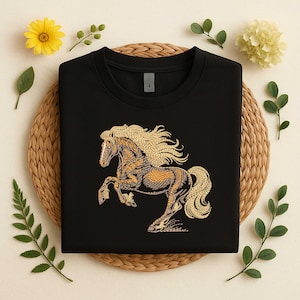 May include: Black crew neck sweatshirt featuring a detailed embroidered design of a rearing horse. The horse has a golden mane and tail, with a brown and gold body. The sweatshirt is folded on a woven mat, surrounded by flowers and greenery.
