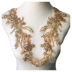 May include: Gold-toned beaded and rhinestone applique. The applique features floral and leaf designs with a mesh backing. The embellishments are arranged in a symmetrical pattern, suitable for embellishing garments or accessories.