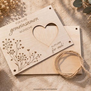 May include: A rectangular light-colored wooden plaque featuring a heart-shaped cutout, engraved floral designs, and the German text "F&Uuml;R EURE gemeinsamen W&Uuml;NSCHE" and "ALLES LIEBE f&uuml;r euch!", accompanied by a separate wooden board and a length of jute twine.