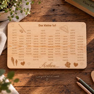 May include: A rectangular wooden board featuring a laser-engraved multiplication table titled Das kleine 1x1. The board includes illustrations of a pencil, a protractor, ice cream cones, and a backpack, with the name Anthea engraved at the bottom center.