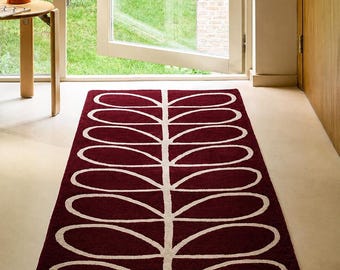 Puede incluir: Una alfombra de pasillo burdeos con un diseño blanco en forma de hojas. La alfombra es rectangular y está colocada en un pasillo, con una puerta y una ventana visibles en el fondo. El diseño es una serie repetida de óvalos alargados y conectados.