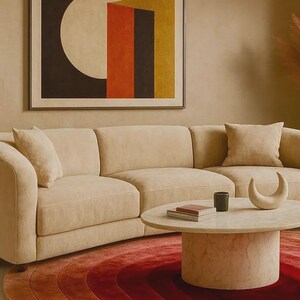 Close-up detail of a luxury hand-tufted silk gradient area rug in rich ombre tones of deep burgundy, crimson red, and terracotta rose, styled beneath a round travertine marble coffee table and a curved cream bouclé sectional sofa. The concentric arch pattern and plush pile texture are prominently visible, complemented by a bold mid-century modern wall art in the background. Ideal statement rug for warm-toned contemporary living spaces. Available in 6x9 and 8x10.