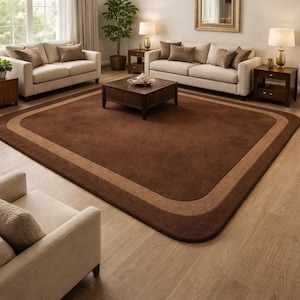 May include: A large, rectangular brown area rug with a lighter brown border. The rug is placed in a living room setting with beige sofas, wooden furniture, and a hardwood floor. The room is well-lit with natural light.